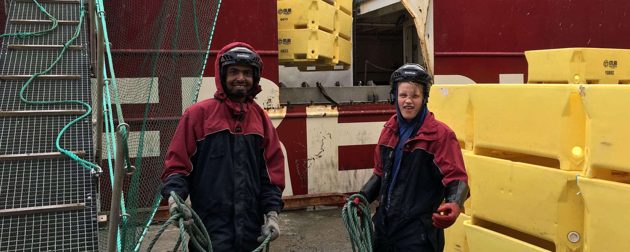 To mannskap i arbeidsdress og hjelm med tau på dekk